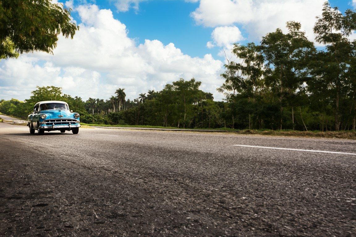 Classic car driving along an empty road in Cuba