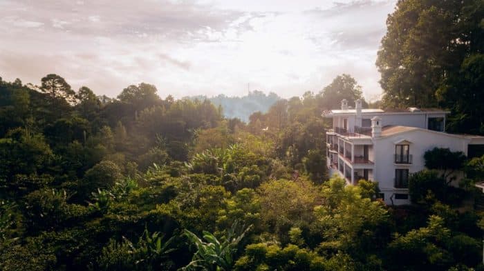 A white building on the right overlooking a misty forest in Guatemala